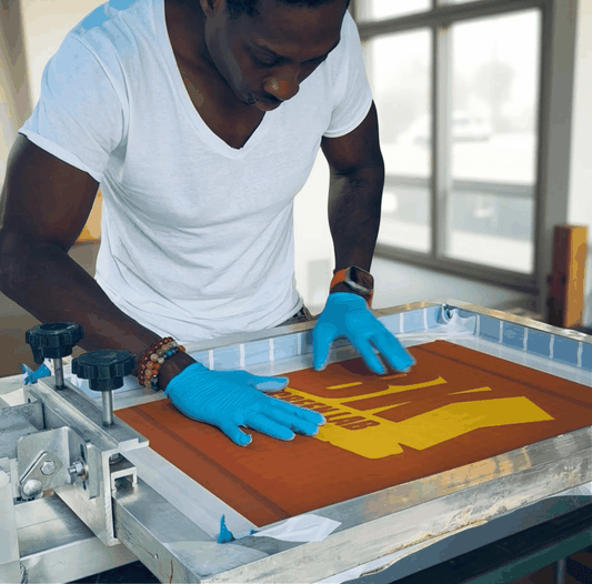 Man in gloves working on screen printing with orange ink at a Screen Print Work Shop